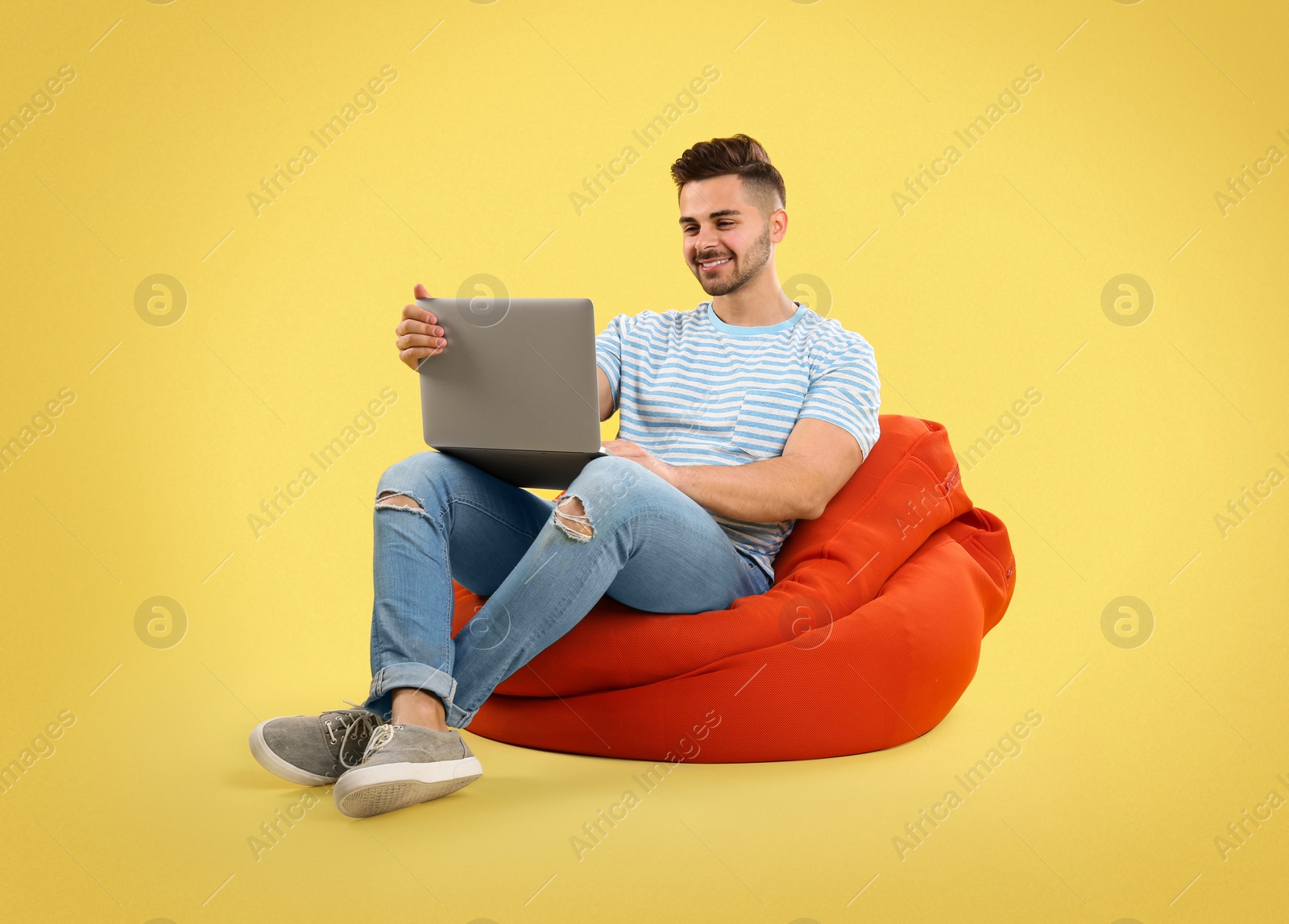 Image of Young man with laptop on bean bag chair, yellow background