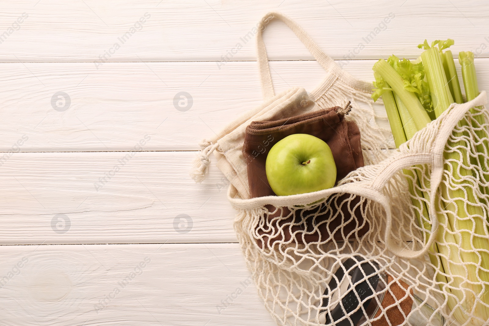 Photo of Net bag with different items on white wooden table, top view and space for text. Conscious consumption