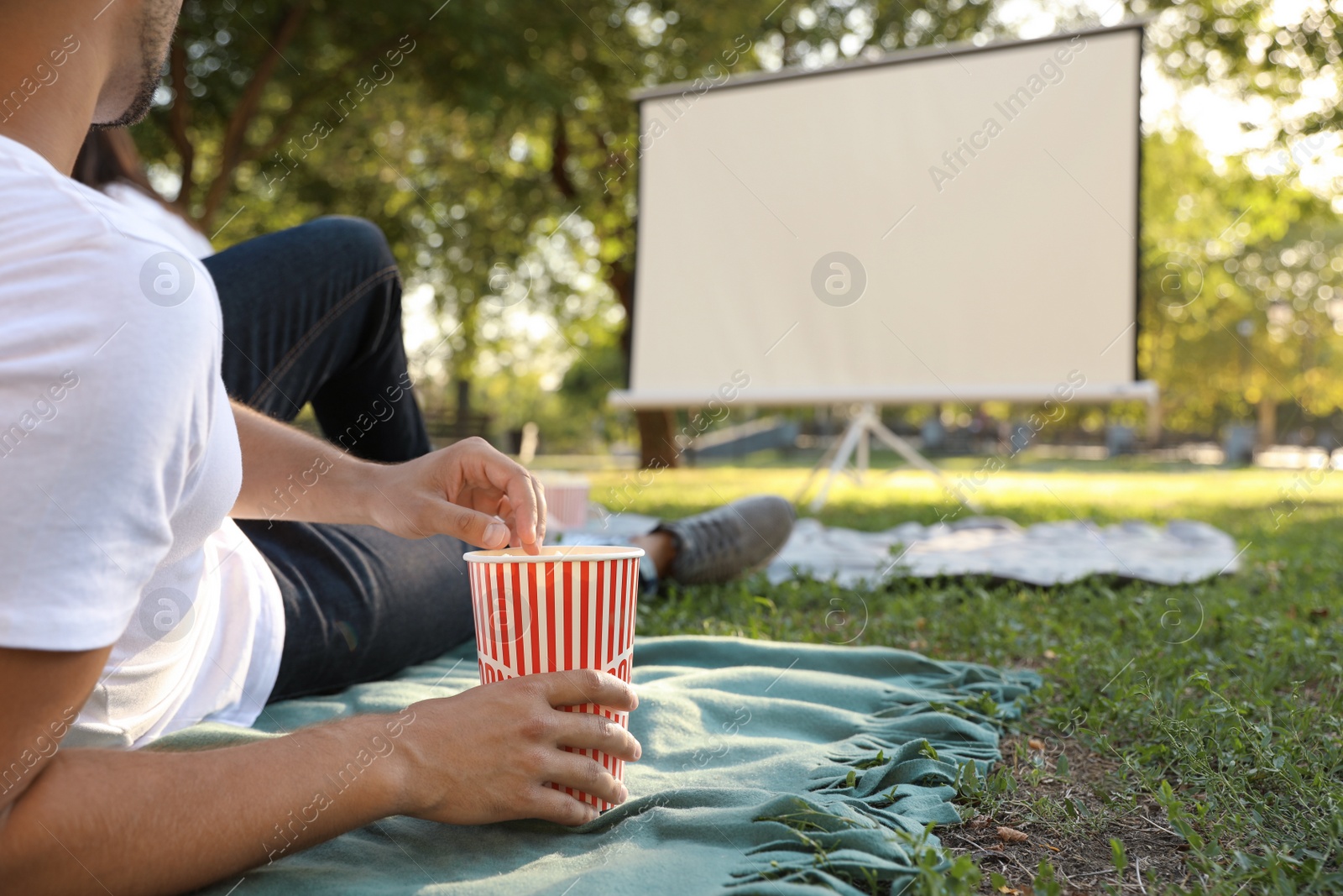 Photo of Young man with popcorn watching movie in open air cinema, closeup. Space for text