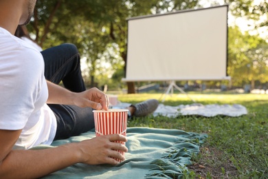 Photo of Young man with popcorn watching movie in open air cinema, closeup. Space for text