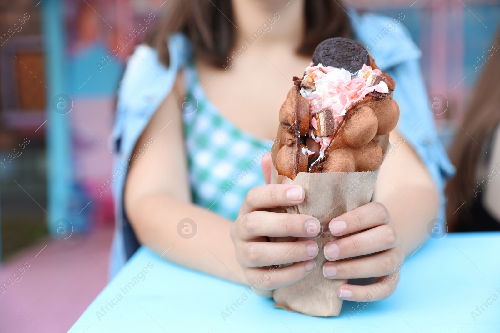 Photo of Young woman holding delicious sweet bubble waffle with ice cream at table outdoors, closeup