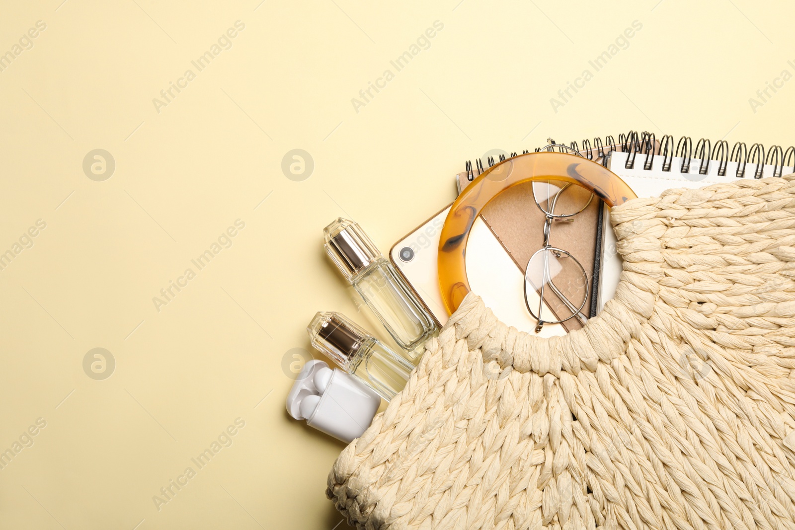 Photo of Stylish woman's bag with smartphone and accessories on light yellow background, flat lay