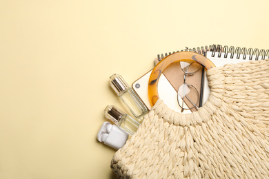 Stylish woman's bag with smartphone and accessories on light yellow background, flat lay