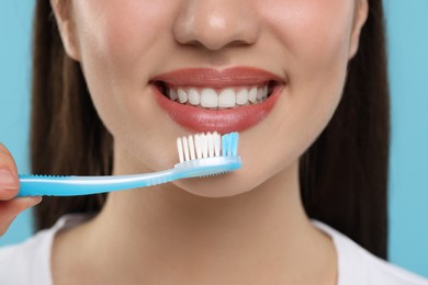 Photo of Woman brushing her teeth with plastic toothbrush on light blue background, closeup