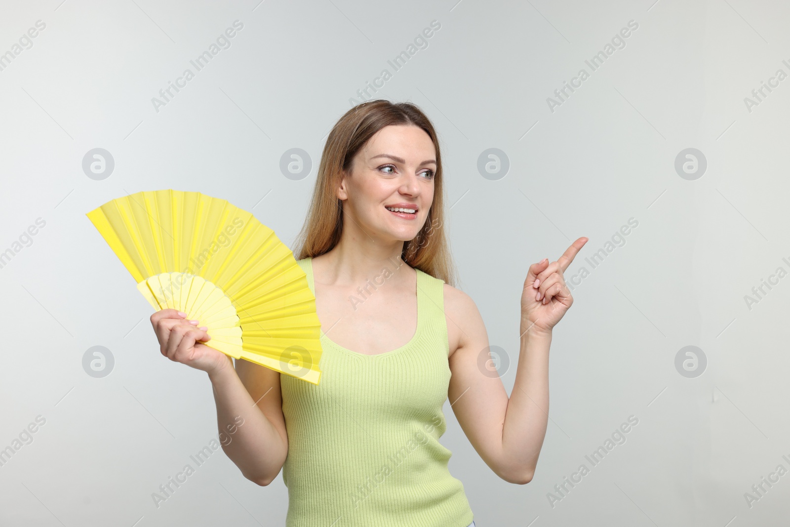 Photo of Happy woman with yellow hand fan pointing on light grey background