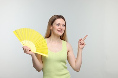 Photo of Happy woman with yellow hand fan pointing on light grey background