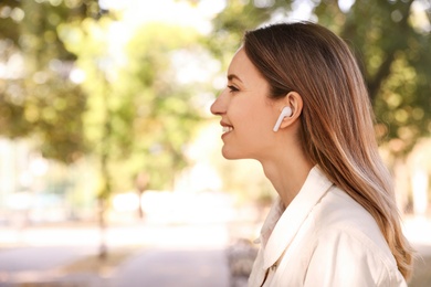 Young woman with wireless headphones listening to music in park. Space for text