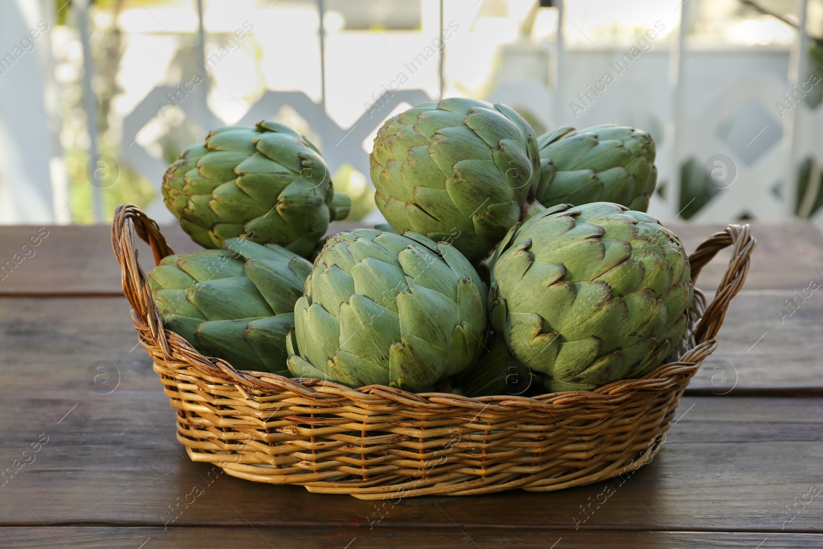 Photo of Wicker basket with fresh raw artichokes on wooden table