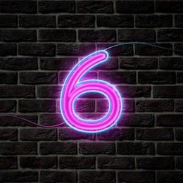 Glowing neon number 6 sign on brick wall