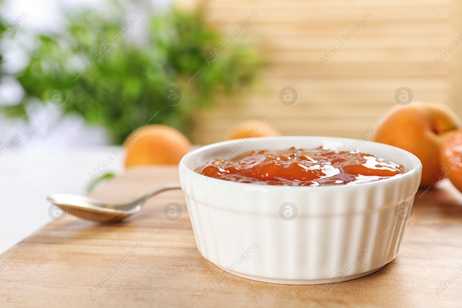 Photo of Bowl with tasty apricot jam on wooden board