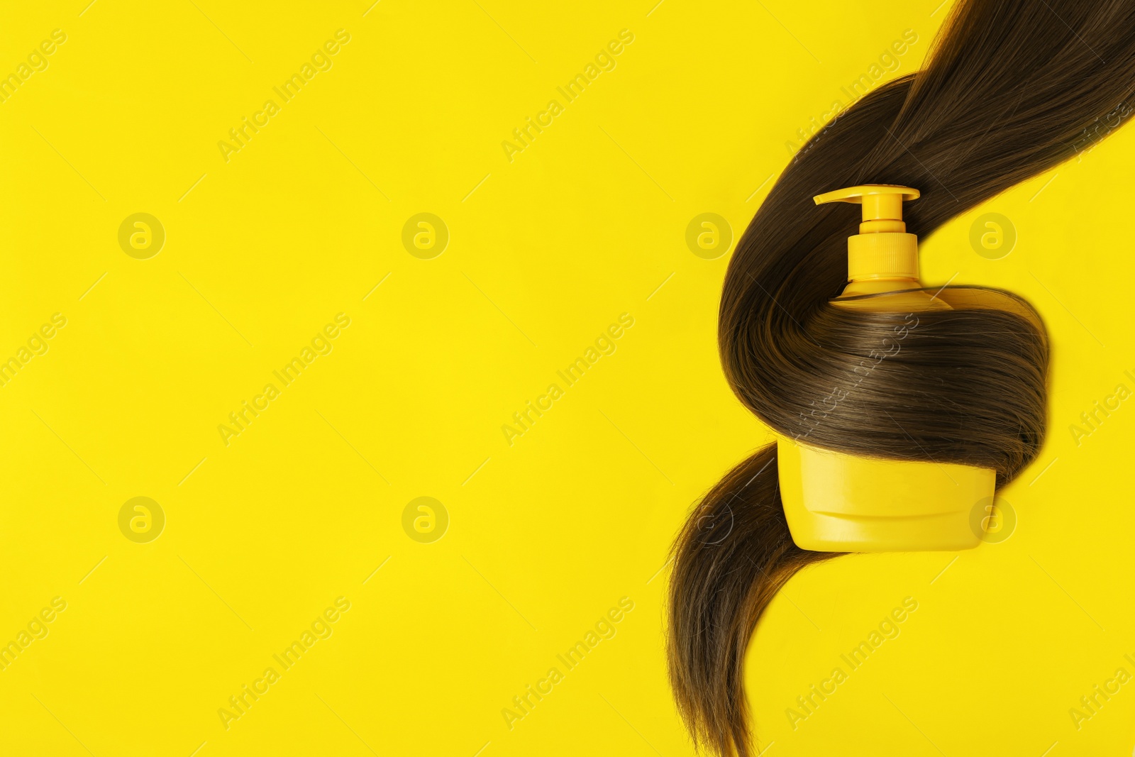 Photo of Shampoo bottle wrapped in lock of hair on yellow background, flat lay with space for text. Natural cosmetic products