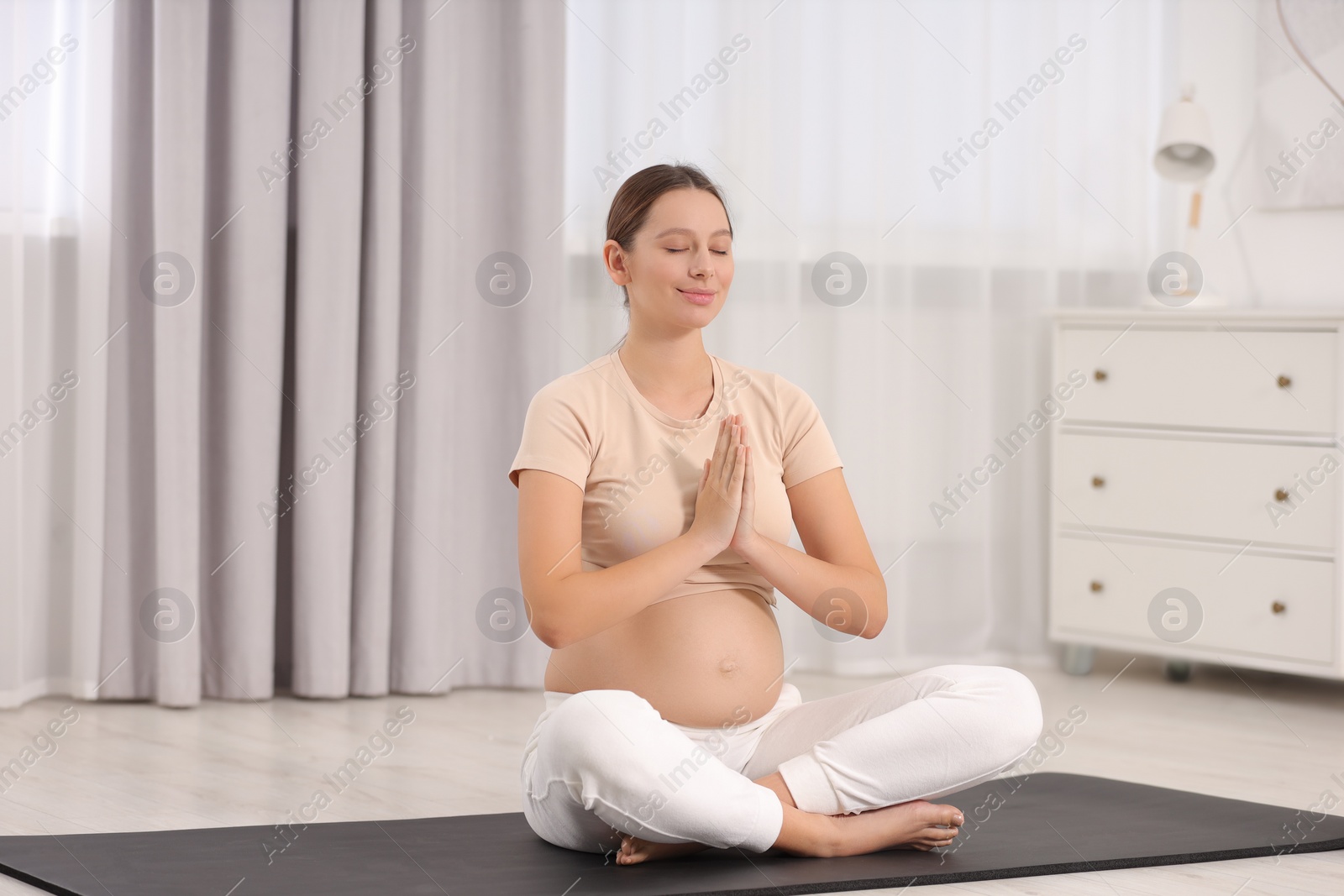 Photo of Pregnant woman meditating on yoga mat at home