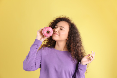 Beautiful African-American woman with donut on yellow background