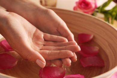Photo of Woman soaking her hands in bowl of water and petals, closeup with space for text. Spa treatment