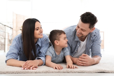 Photo of Happy couple and their son lying on carpet at home. Family time