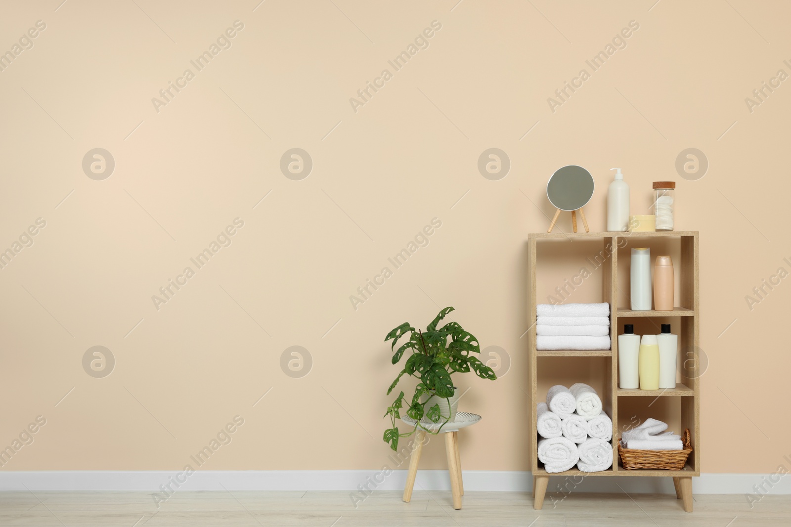 Photo of Soft folded towels and cosmetic bottles on wooden shelving unit near beige wall, space for text