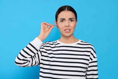 Photo of Young woman cleaning ear with cotton swab on light blue background