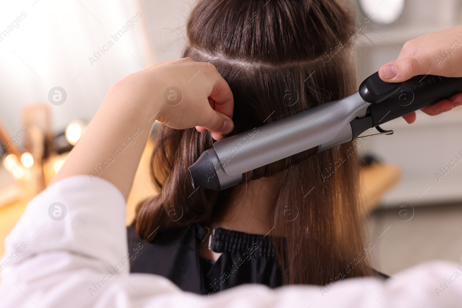 Photo of Hairdresser curling woman's hair with iron in salon, closeup