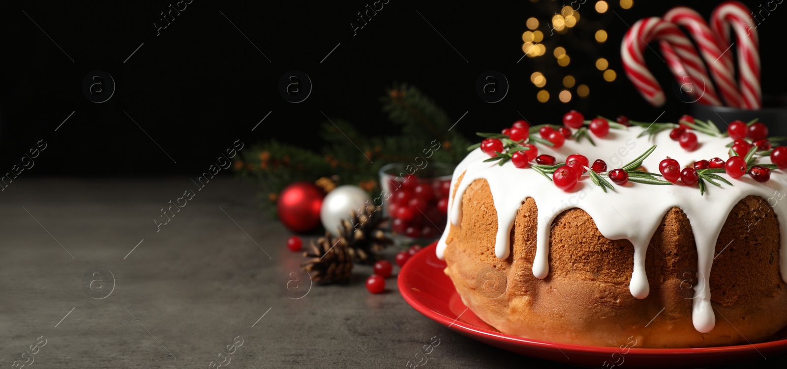 Image of Traditional Christmas cake decorated with glaze, pomegranate seeds, cranberries and rosemary on grey table, space for text. Banner design