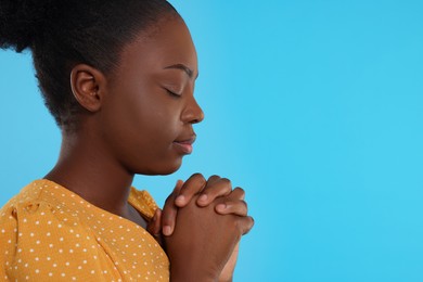 Photo of Woman with clasped hands praying to God on light blue background. Space for text