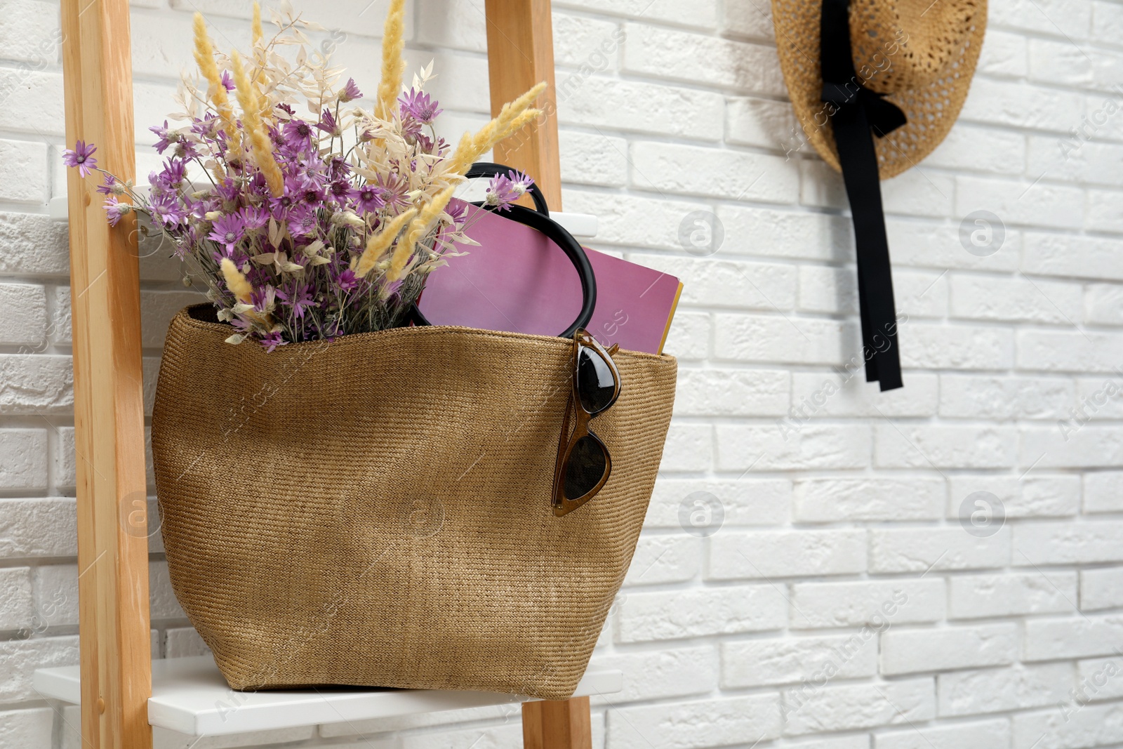 Photo of Stylish beach bag with beautiful bouquet of wildflowers, sunglasses and magazines on shelf indoors. Space for text