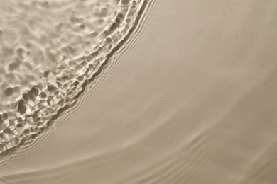 Rippled surface of clear water on beige background, top view