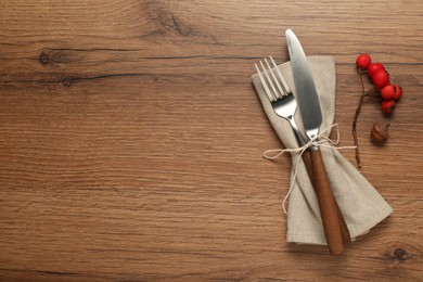 Photo of Napkin, cutlery and berries on wooden background, flat lay with space for text. Stylish autumn table setting