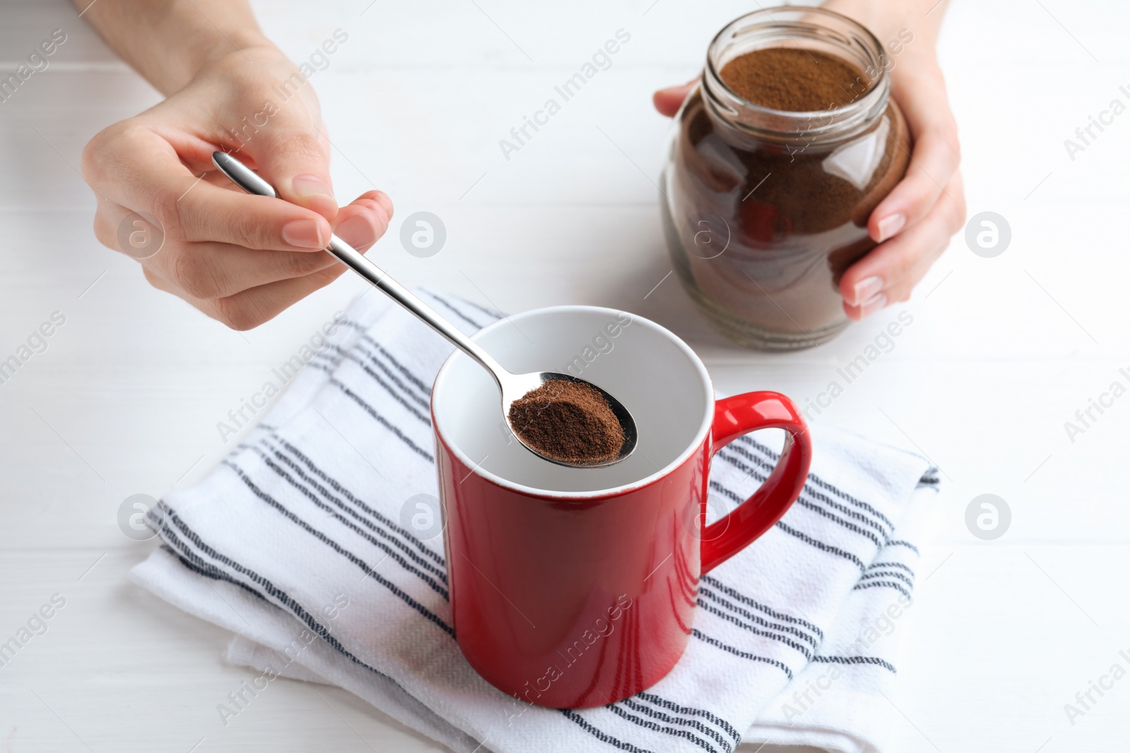 Photo of Woman pouring instant coffee into mug at white table, closeup