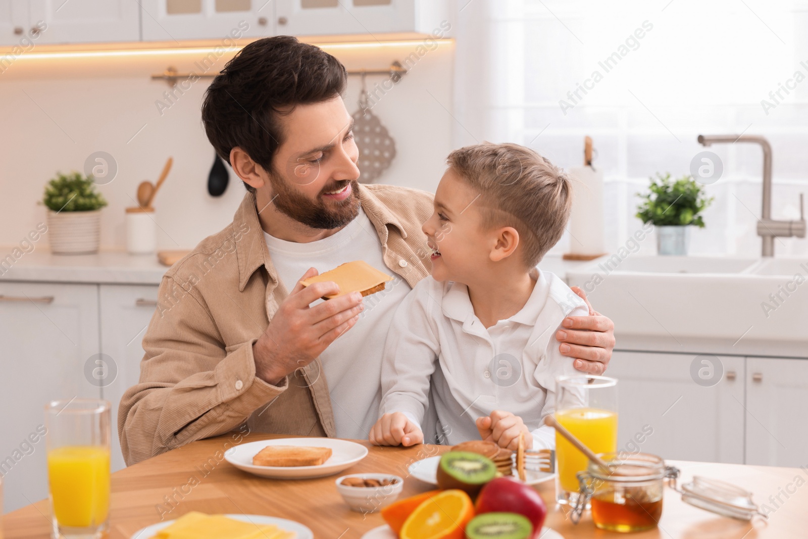 Photo of Father and his cute little son having breakfast at table in kitchen