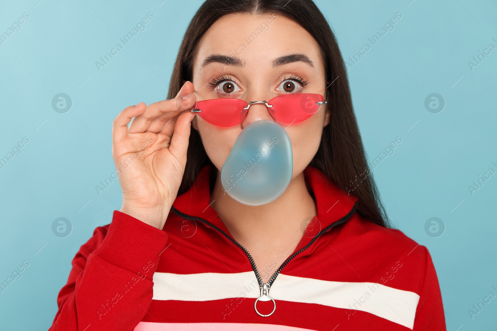 Photo of Beautiful young woman blowing bubble gum on light blue background