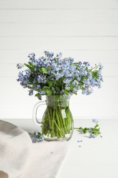 Bouquet of beautiful forget-me-not flowers in glass jug and blue cloth on white table