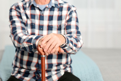 Photo of Elderly man with walking cane sitting on bed, closeup. Space for text