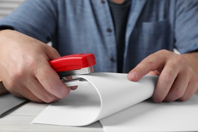 Man with papers using stapler at white wooden table, closeup