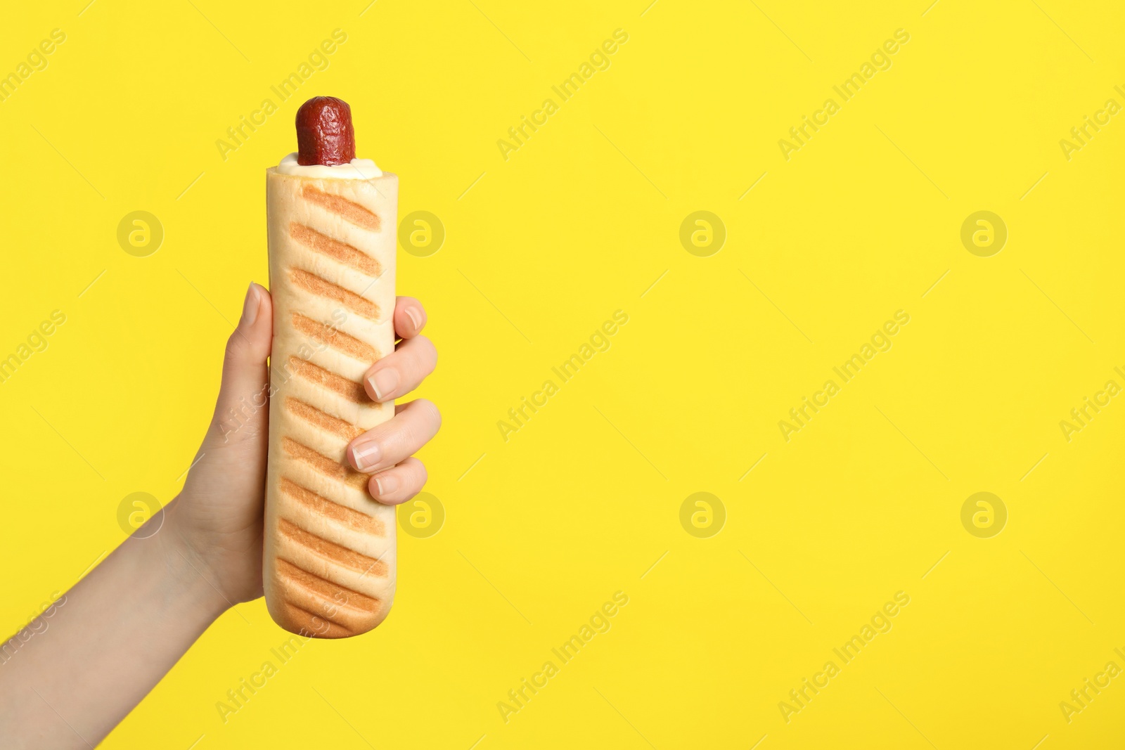 Photo of Woman holding delicious french hot dog on yellow background, closeup. Space for text