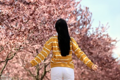 Photo of Young woman near beautiful blossoming trees outdoors, back view. Stylish spring look