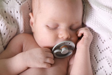 Cute newborn baby with pacifier sleeping on white blanket, closeup