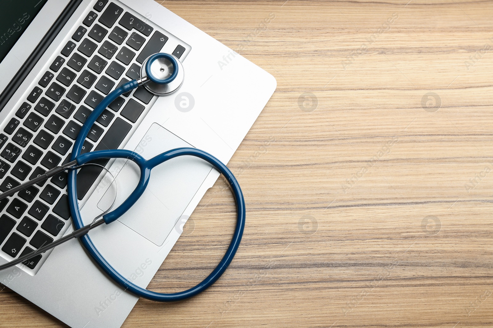 Photo of Laptop and stethoscope on wooden table, flat lay with space for text. Concept of technical support