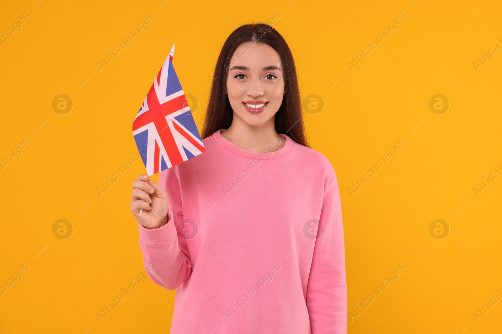 Photo of Young woman holding flag of United Kingdom on orange background