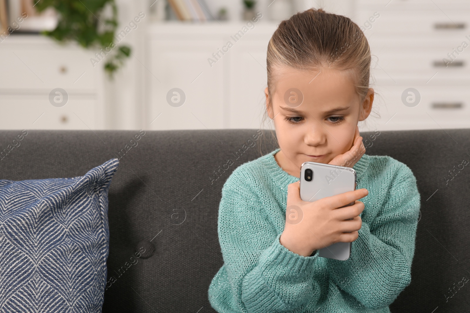 Photo of Little girl using smartphone on sofa at home. Internet addiction