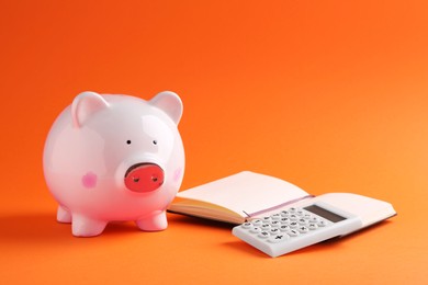 Financial savings. Piggy bank, notebook and calculator on orange background