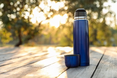 Photo of Modern blue thermos on wooden surface outdoors. Space for text