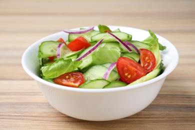 Bowl of tasty salad with cucumber, tomato and lettuce on table