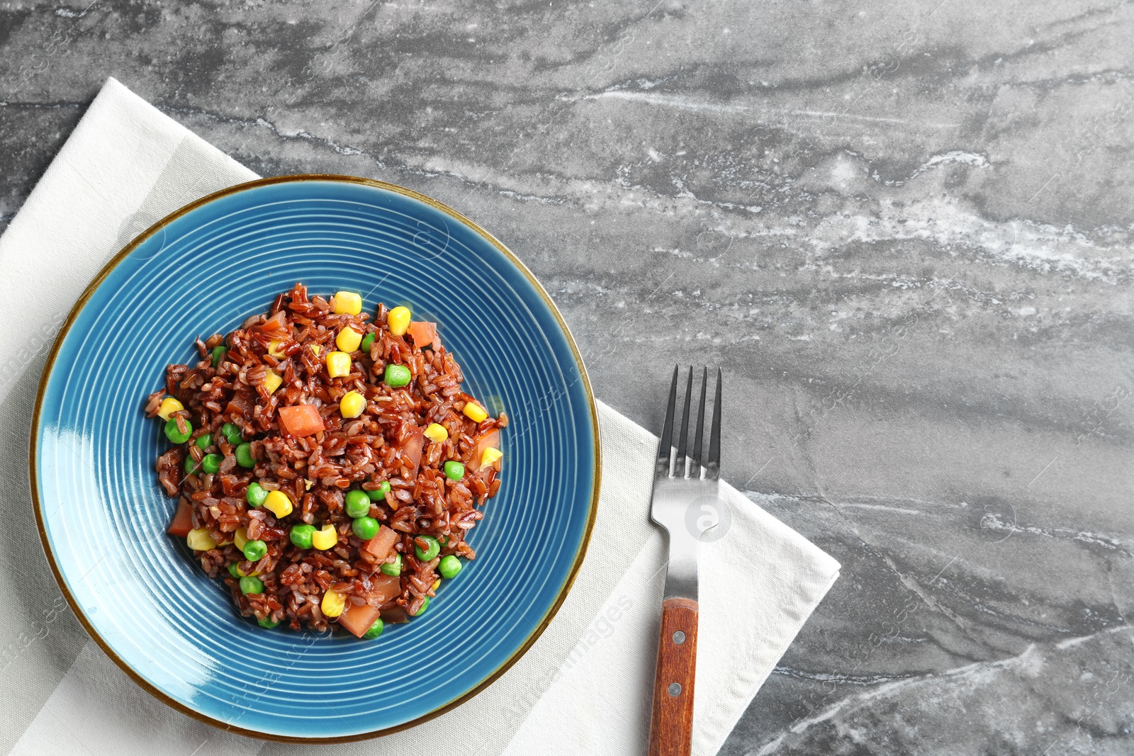 Photo of Plate of boiled brown rice with vegetables served on table, top view. Space for text