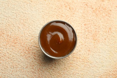 Photo of Tasty barbeque sauce in bowl on beige textured table, top view