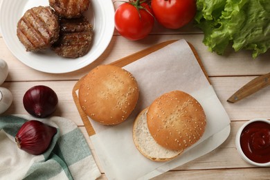 Delicious fried patties, vegetables, buns and sauce on light wooden table, flat lay. Making hamburger