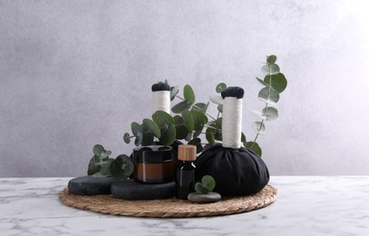 Photo of Spa composition with cosmetic products, herbal massage bags, stones and eucalyptus branches on white marble table