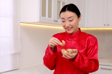 Photo of Asian woman holding bowl of tasty fortune cookies with predictions in kitchen. Space for text