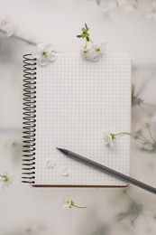 Guest list. Notebook, pencil and beautiful cherry tree blossoms on spring floral background, flat lay