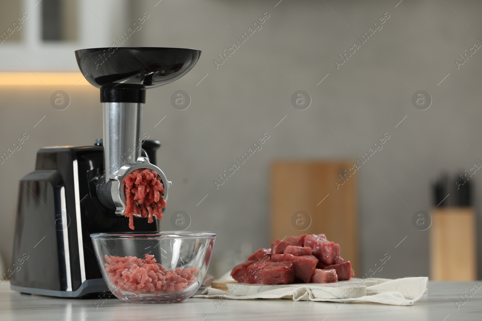 Photo of Electric meat grinder with beef mince on white table in kitchen