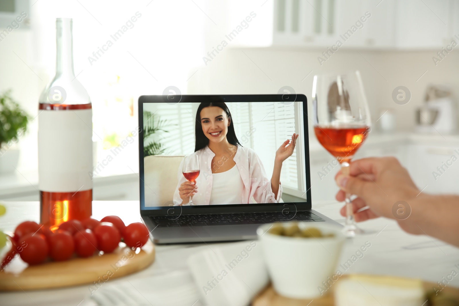 Photo of Friends drinking wine while communicating through online video conference in kitchen. Social distancing during coronavirus pandemic